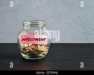 Vaso di vetro con monete e la parola di investimento su un'etichetta. Investire in un nuovo progetto di business o immobiliare. Risparmio di denaro. Accumulazione di capitale, distro Foto Stock