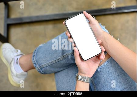 Vista dall'alto, Le mani di Un uomo che tiene un moderno smartphone in grembo. Schermo bianco del telefono mockup. Immagine ravvicinata Foto Stock