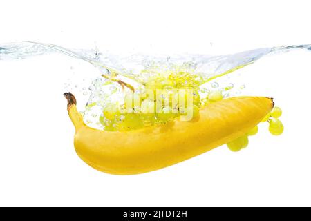 Banana e mazzo di uve bianche che spruzzano in acqua isolato su fondo bianco. Foto Stock