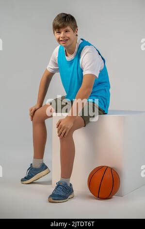 Un ragazzo soddisfatto seduto su un cubo e sorridente Foto Stock