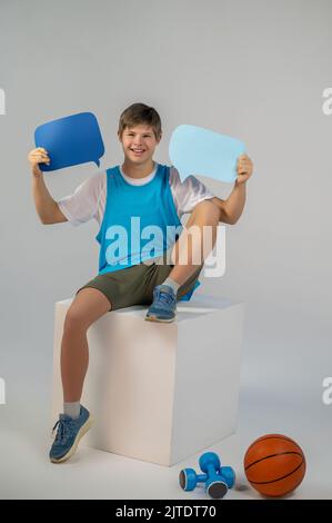 Un ragazzo sorridente seduto su un cubo con i segni dei commenti nelle mani Foto Stock