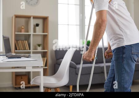 Un giovane che ha disabilità o una gamba ferita rotta cammina sulle stampelle a casa Foto Stock