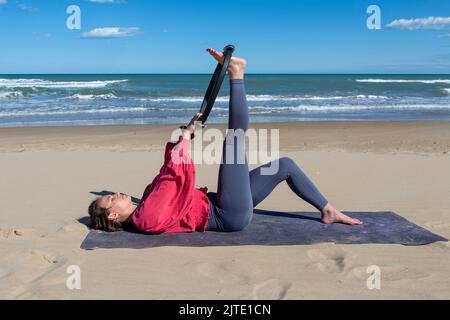 bella donna che si esercita sulla spiaggia con pilates anello Foto Stock