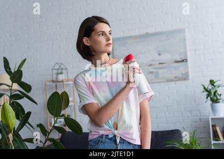 Donna spruzzante deodorante per ambienti vicino alle piante a casa Foto Stock