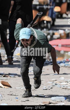 Baghdad, Iraq. 30th ago, 2022. Membro armato di Saraya al-Salam, l'ala militare collegata al clerico sciita iracheno Muqtada al-Sadr si copre durante gli scontri con le forze di sicurezza irachene nella zona verde dell'Iraq. Fonti di sicurezza e assistenza medica irachene hanno riferito che almeno 25 persone sono state uccise e 450 feriti dopo i disordini scoppiati il giorno precedente. Credit: Ameer al-Mohammedawi/dpa/Alamy Live News Foto Stock