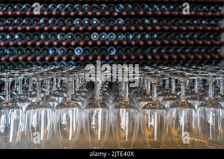 Bicchieri da vino vuoti con molte bottiglie impilate come sfondo - preparazione alla degustazione di vini nella cantina di Lanzarote, Spagna Foto Stock