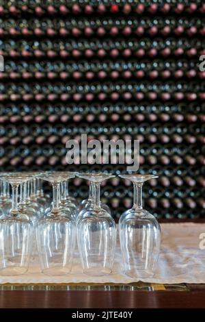 Bicchieri da vino vuoti con molte bottiglie impilate come sfondo - preparazione alla degustazione di vini nella cantina di Lanzarote, Spagna Foto Stock