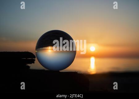 Ammira il tramonto sulla costa dell'oceano attraverso una palla di vetro. Messa a fuoco selettiva. Foto Stock