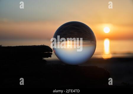 Ammira il tramonto sulla costa dell'oceano attraverso una palla di vetro. Messa a fuoco selettiva. Foto Stock