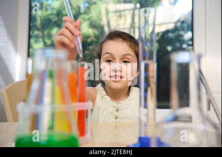 La studentessa ispirata che utilizza la pipetta, fa esperimenti di laboratorio sulla lezione di chimica. Vetreria da laboratorio in primo piano sfocato Foto Stock