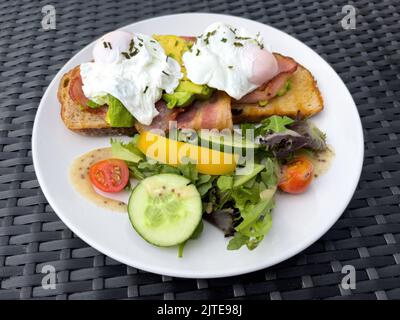 Colazione sana con uova in camicia, pancetta alla griglia e avocado servita su una fetta di pane tostato Foto Stock