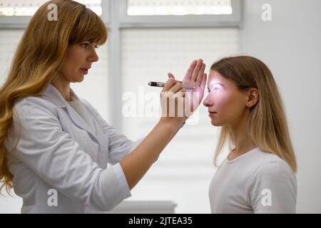 Medico di sesso femminile che controlla gli occhi della giovane paziente con il fashlight. Diagnosi di malattie neurologiche Foto Stock