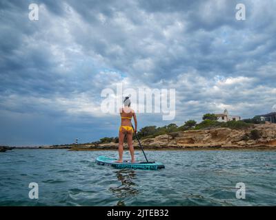 Donna in tavola da surf sotto un cielo drammatico, Estalella, costa di Llucmajor, Maiorca, Isole Baleari, Spagna Foto Stock