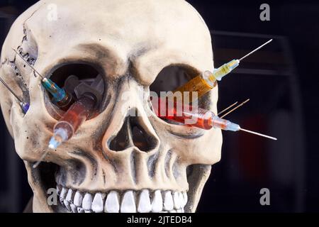 Cranio umano con siringhe riempite di liquido colorato. Concetto di pericolo di droga. Isolato su sfondo nero. Foto Stock