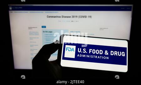 Persona che tiene il cellulare con il logo della Food and Drug Administration (FDA) degli Stati Uniti sullo schermo di fronte alla pagina web. Messa a fuoco sul display del telefono. Foto Stock