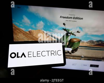 Persona che tiene il telefono cellulare con il logo della società indiana Ola Electric Mobility Pvt. Ltd. Sullo schermo davanti alla pagina Web. Messa a fuoco sul display del telefono. Foto Stock