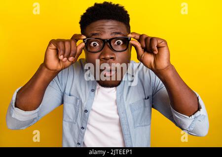 Foto di giovane brunetta impressionato Guy look fotocamera indossare occhiali jeans camicia isolato su sfondo di colore giallo Foto Stock