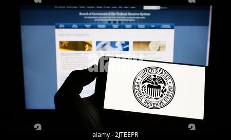 Persona che tiene il cellulare con sigillo di United States Federal Reserve System (FED) sullo schermo di fronte al sito web. Messa a fuoco sul display del telefono. Foto Stock