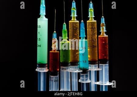 Siringhe per primo piano con medicinali colorati isolate su sfondo nero. Concetto di vaccinazione e trattamento. Foto Stock