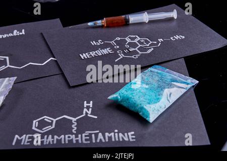 Fogli con eroina e metamfetamina molecole di droga su sfondo nero. Siringa riempita con eroina e confezione di meto blu. Foto Stock