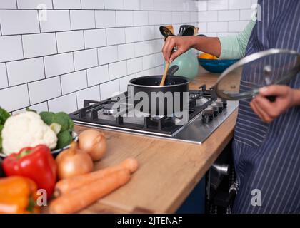 Primo piano di una giovane donna che agita una pentola di cibo su stovetop a gas Foto Stock