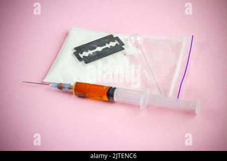 Siringa con rasoio e confezione di polvere su sfondo rosa. Uso di droghe per iniezione. Foto Stock