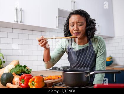 Una giovane donna multirazziale assaggia la sua cucina ed è incerto del sapore Foto Stock