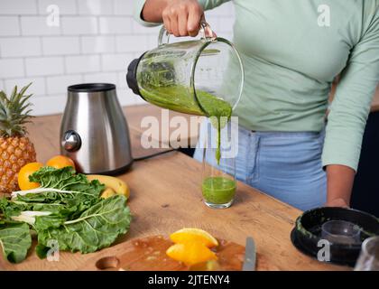 Primo piano della donna che versa frullato verde fatto in casa in vetro Foto Stock