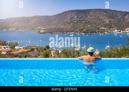 Un turista in piscina gode della vista delle barche a vela in una baia dell'isola di Poros Foto Stock