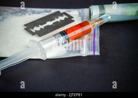 Siringa per primo piano riempita di farmaco con rasoio e confezione di cocaina. Concetto di dipendenza dalla droga. Foto Stock