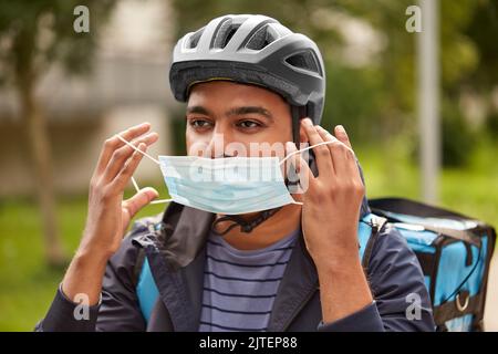 consegna di cibo uomo in maschera e casco da bicicletta Foto Stock