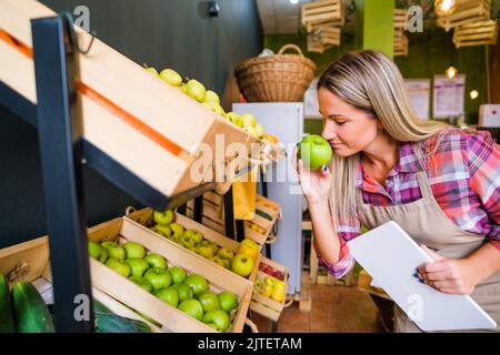 Donna lavora nel negozio di frutta e verdura. Sta esaminando le merci nei cestini. Foto Stock