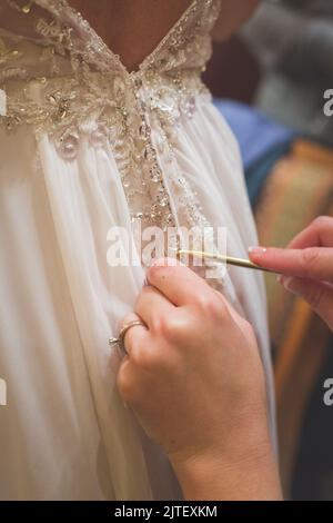 Sposa essere aiutato in vestito di nozze da bridessmaid usando un ago di maglia. Foto Stock