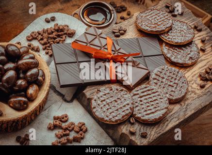 Composizione di diverse barrette e pezzi di cioccolato fondente, cioccolato fuso e chicchi di caffè su sfondo di legno antico. Messa a fuoco selettiva. Foto Stock