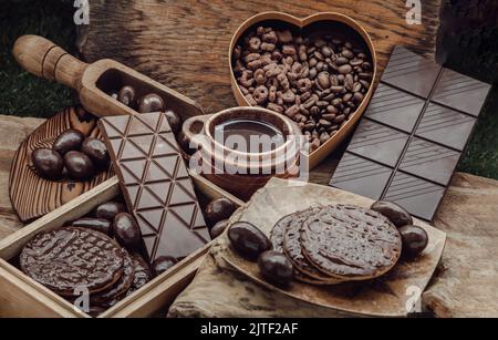 Composizione di diverse barrette e pezzi di cioccolato fondente, cioccolato fuso e chicchi di caffè su sfondo di legno antico. Messa a fuoco selettiva. Foto Stock