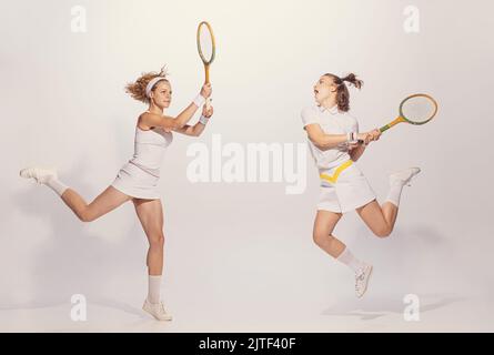 Ritratto di due giovani donne attive in uniforme retrò giocando badminton isolato su sfondo grigio studio Foto Stock