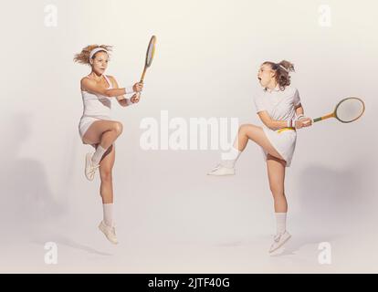 Ritratto di giovani donne in uniforme retro giocando badminton con racchette di legno isolato su sfondo grigio studio Foto Stock