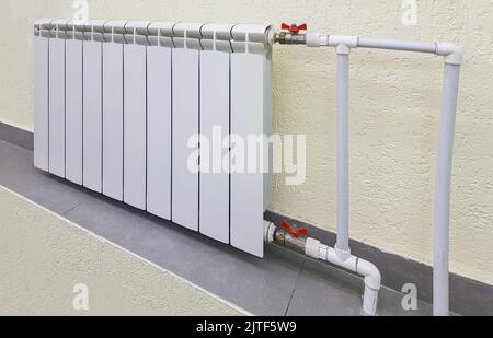 Moderna batteria bianca in alluminio per il riscaldamento dell'acqua calda, sullo sfondo di una parete all'interno di un appartamento o di uno spazio ufficio. Foto Stock