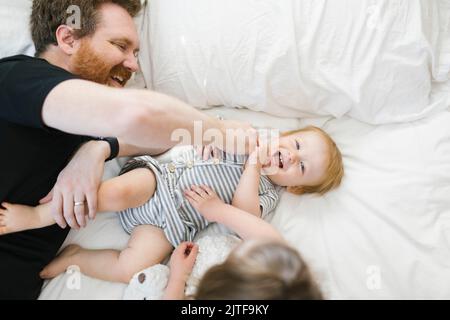 Padre che gioca con il figlio (12-17 mesi) e la figlia (2-3) a letto Foto Stock