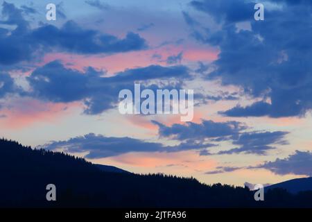 Bagliore rosa su nuvole alte dopo il tramonto con la linea dell'albero in primo piano in ombra Foto Stock