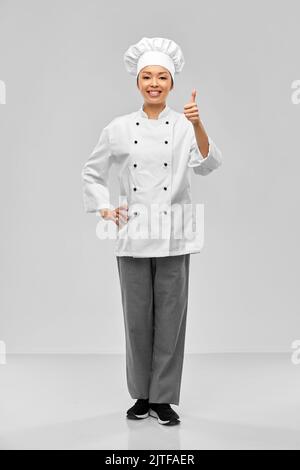 sorridente cuoco femminile in giacca che mostra i pollici in su Foto Stock