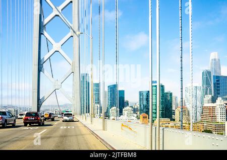 Ci si avvicina a San Francisco sul ponte della baia di Oakland con lo skyline della città visibile sulla destra attraverso i cavi del ponte sospeso. Foto Stock