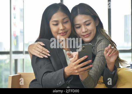Felice due donne asiatiche busimess guardando il telefono cellulare per rilassarsi dopo il lavoro in ufficio Foto Stock