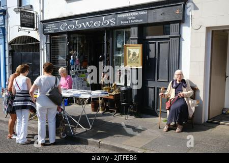 Ballycastle, Regno Unito. 30 agosto 2022. Signora anziana con bastone seduto fuori ragnatele antiquariato. L'ultimo giorno della fiera Ould Lammas. Il giorno di chiusura della fiera più antica d'Irlanda nella cittadina balneare di Ballycastle sulla costa nord di North Antrim, che si conclude con un fine settimana di contrattazione in banca e un programma ricco di intrattenimento, cucina locale e internazionale alla fiera di Ould Lammas. Crediti: Steve Nimmons/Alamy Live News Foto Stock