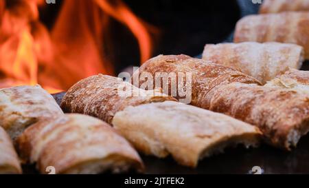 Vista dettagliata ravvicinata dei sandwich grigliati su un barbecue a superficie piana di fronte al fuoco rosso aperto Foto Stock