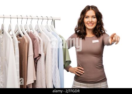 felice assistente di negozio femminile con vestiti su appendiabiti Foto Stock