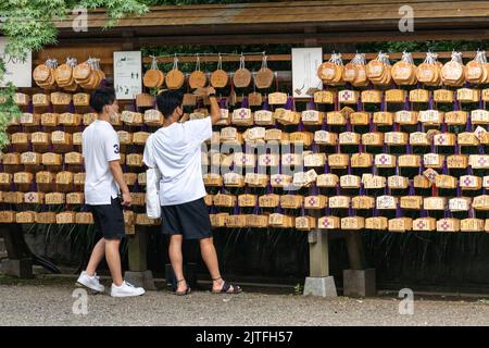 Giovani giapponesi leggono le placche di preghiera Ema al Santuario di Nogi-jinja, a Nogizaka, Akasaka, Tokyo, Giappone. Il piccolo santuario è dedicato al generale Nogi Maresuke e a sua moglie Nogi Shizuko. Foto Stock