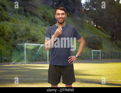 sorridente allenatore di calcio maschile o arbitro con fischio Foto Stock