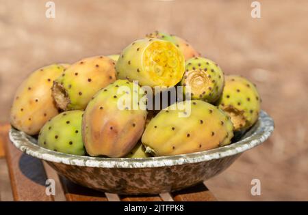 In una ciotola di ceramica si trovano diversi frutti maturi di pera di fico. La ciotola si trova su una base di legno rustico. Foto Stock