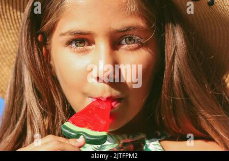 Bella ragazza adolescente mangiare un lecca su un bastone a forma di anguria. Dolci per bambini. Bambino felice con una caramella. Gioia, infanzia, sume Foto Stock